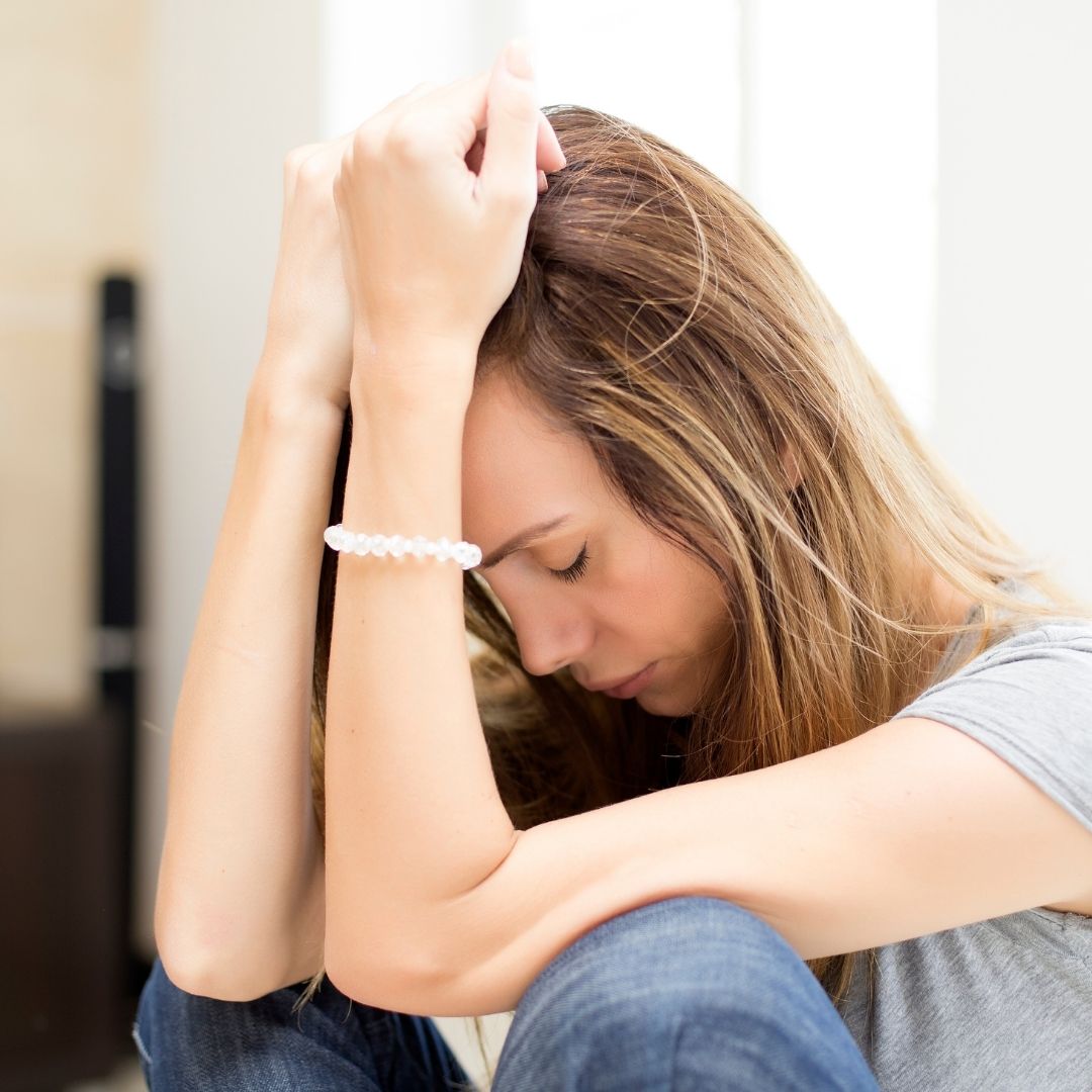 Young woman hanging her head down by her knees locking stressed