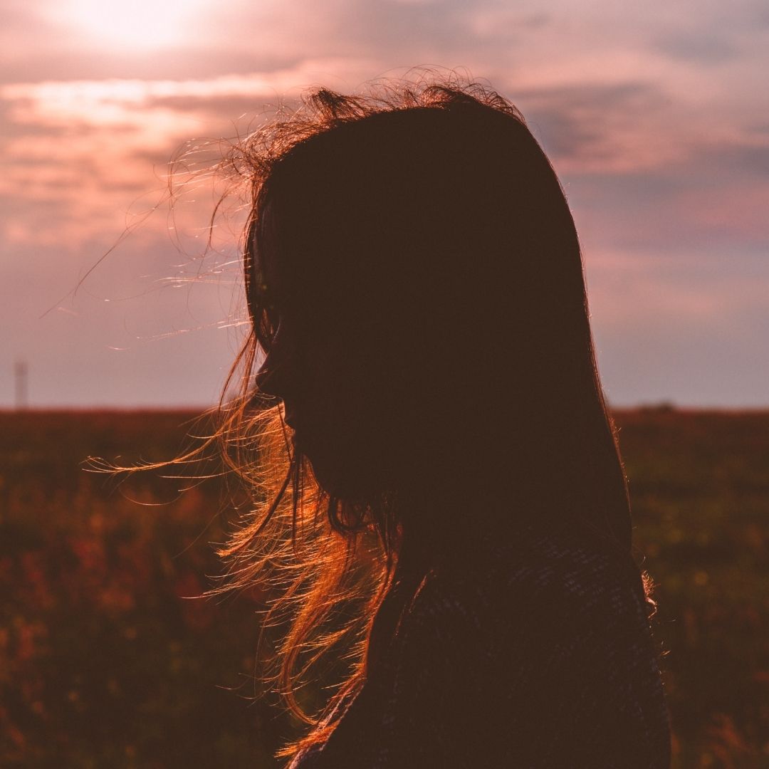 Woman silhouetted by the sun looking stoick as she through a pasture.