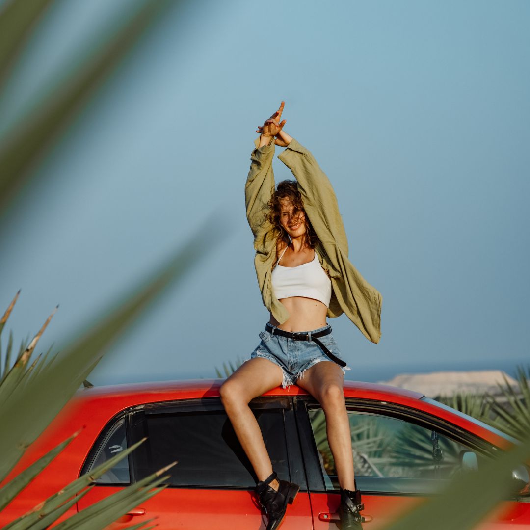 a woman sitting on top of a red car with an excited vibe